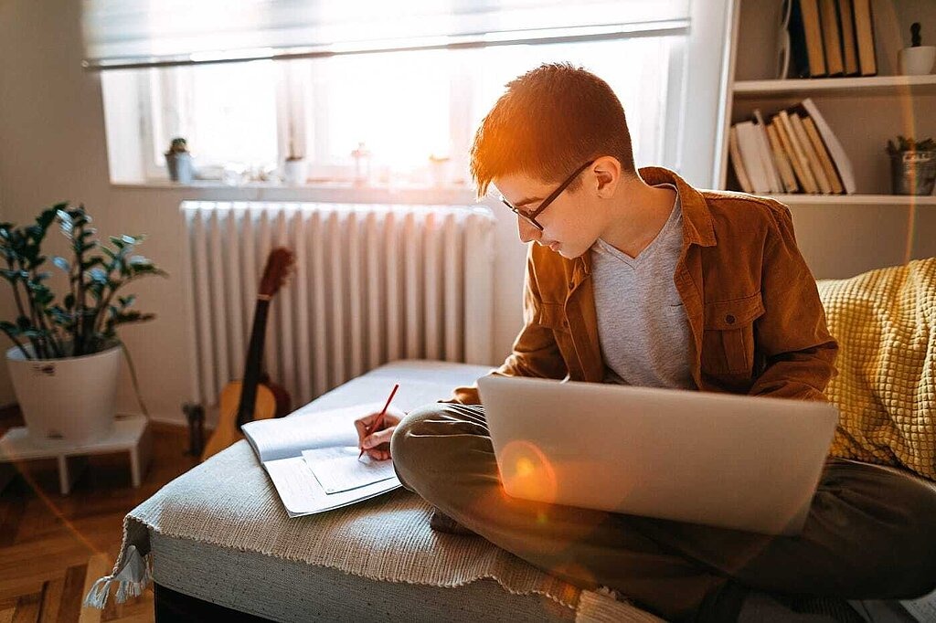 Die perfekte Lernumgebung Junge mit Laptop und Heft auf Sofa