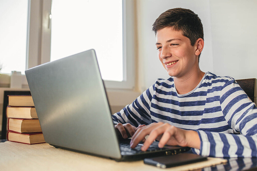 Junge sitzt am Tisch und tippt auf Laptop