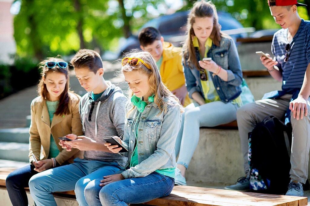 Challanges Social Media Schule Schülerinnen und Schülern auf dem Schulhof schauen auf ihre Smartphones.