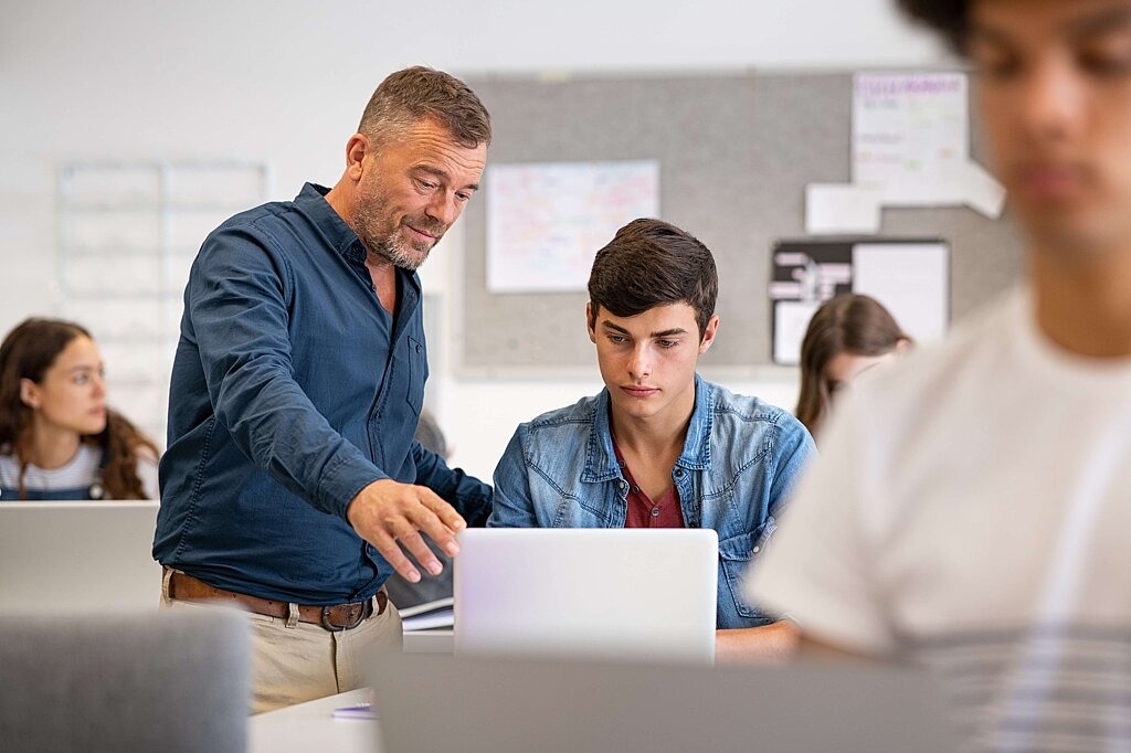 Digitale Lernangebote Lehrer erklärt Schülerinnen und Schülern etwas am Computer.