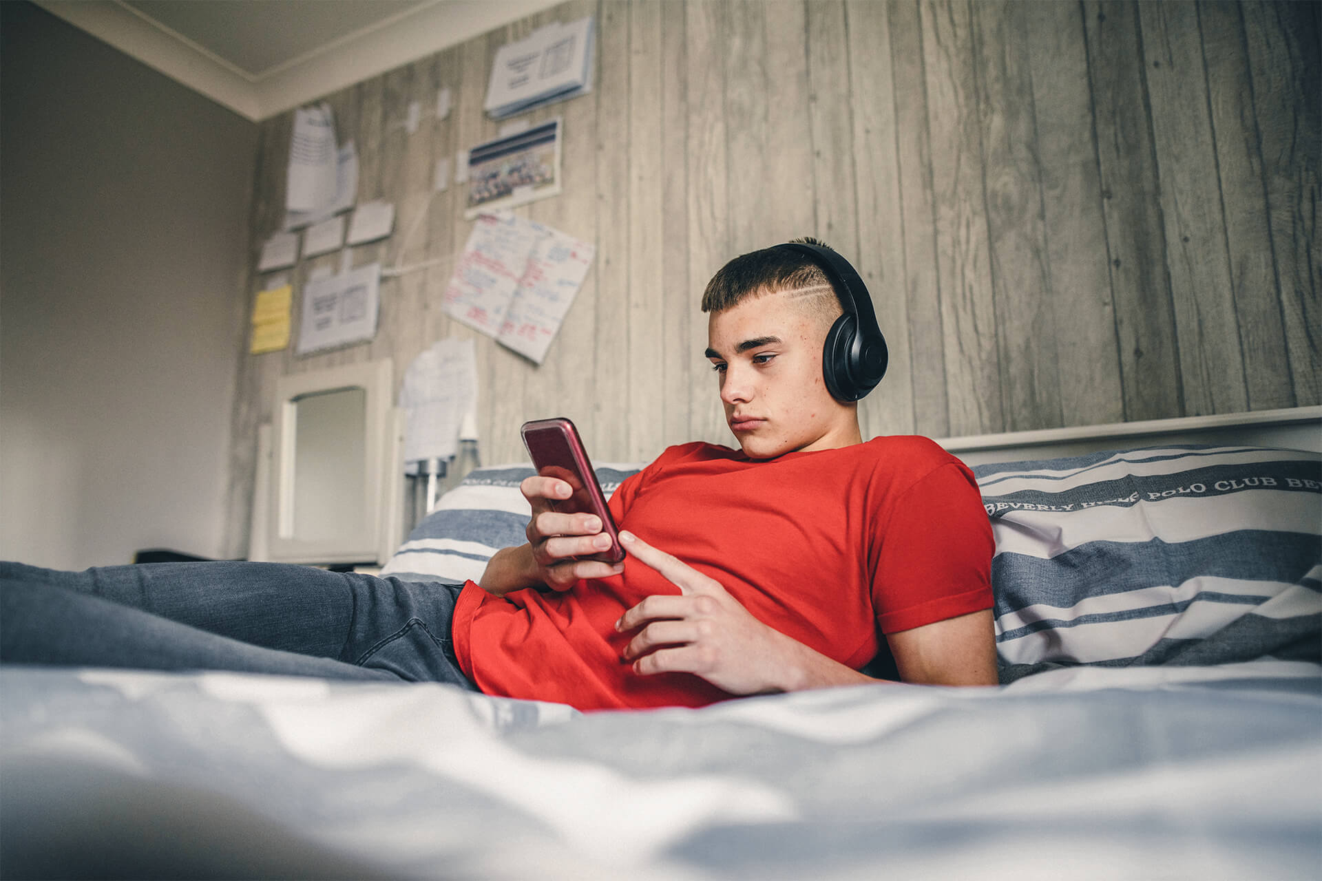 Junge liegt auf Bett mit Kopfhörern und Handy