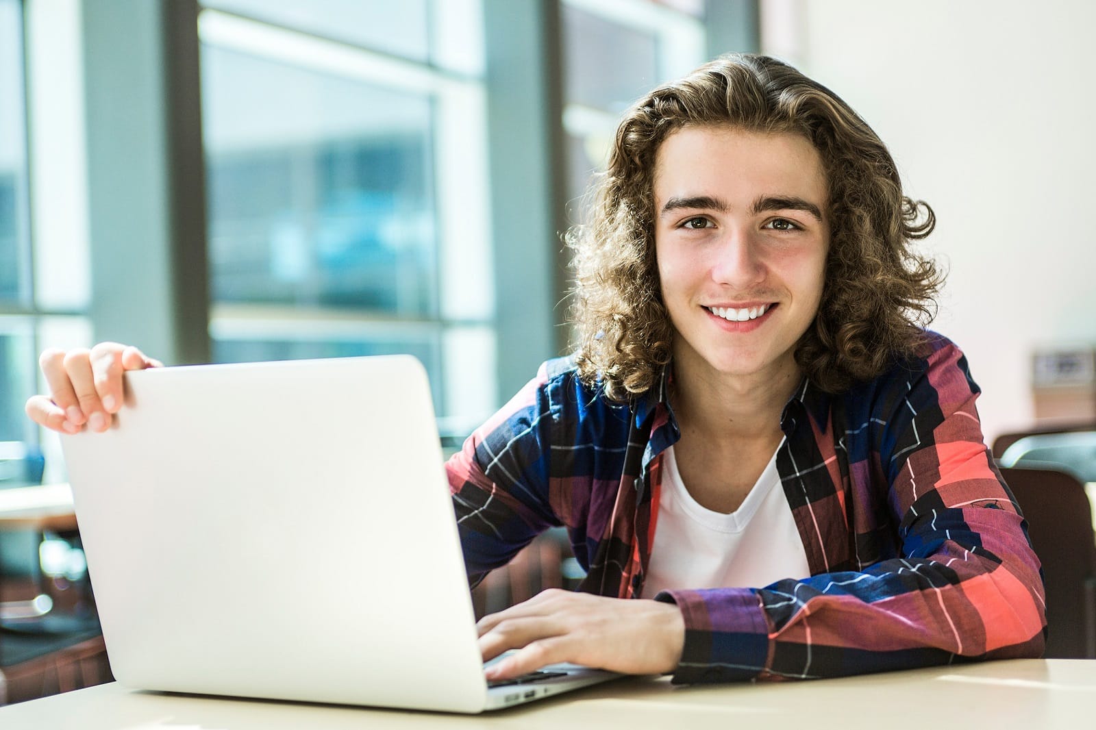 Langhaariger Junge mit Laptop lächelt in die Kamera