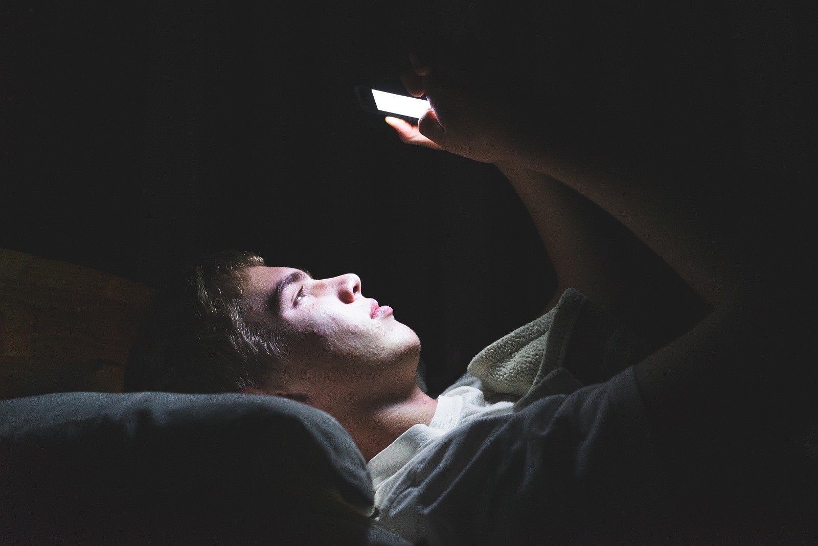 Junge liegt im Dunkeln im Bett und schaut auf Handy