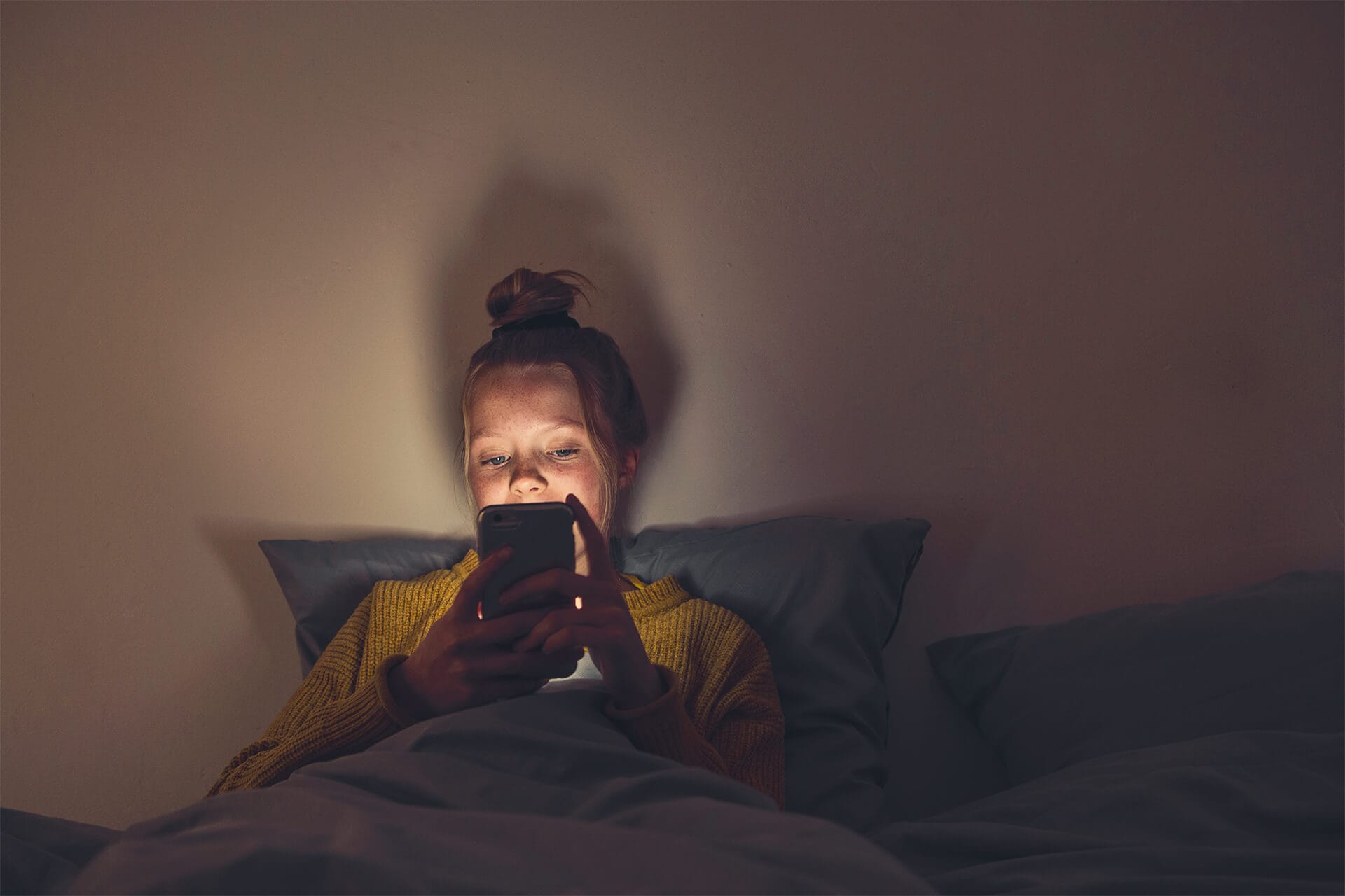 Mädchen im Dunkeln auf Bett, schaut auf Smartphone-Display