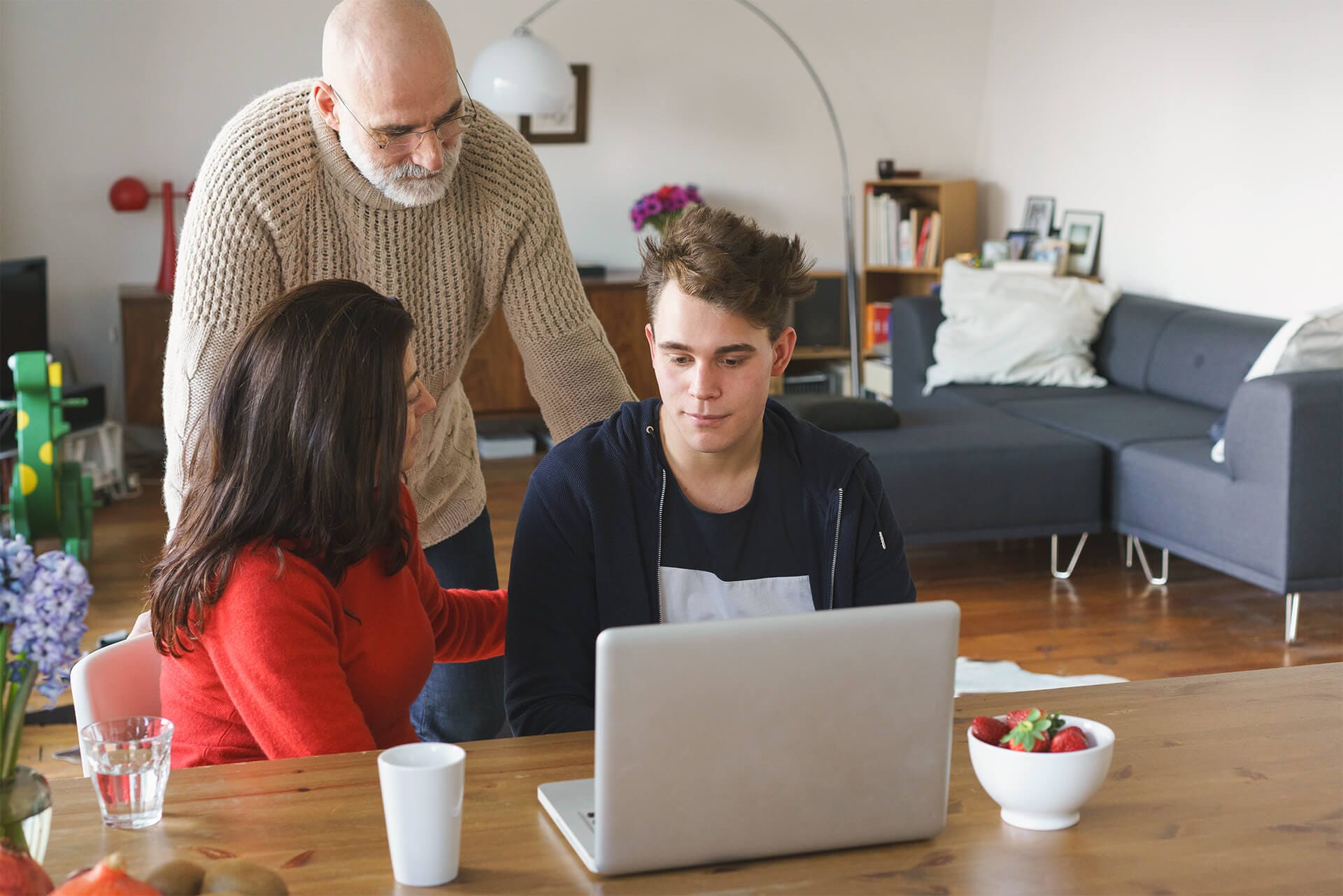 Eltern unterhalten sich mit Sohn, sitzen vor Laptop