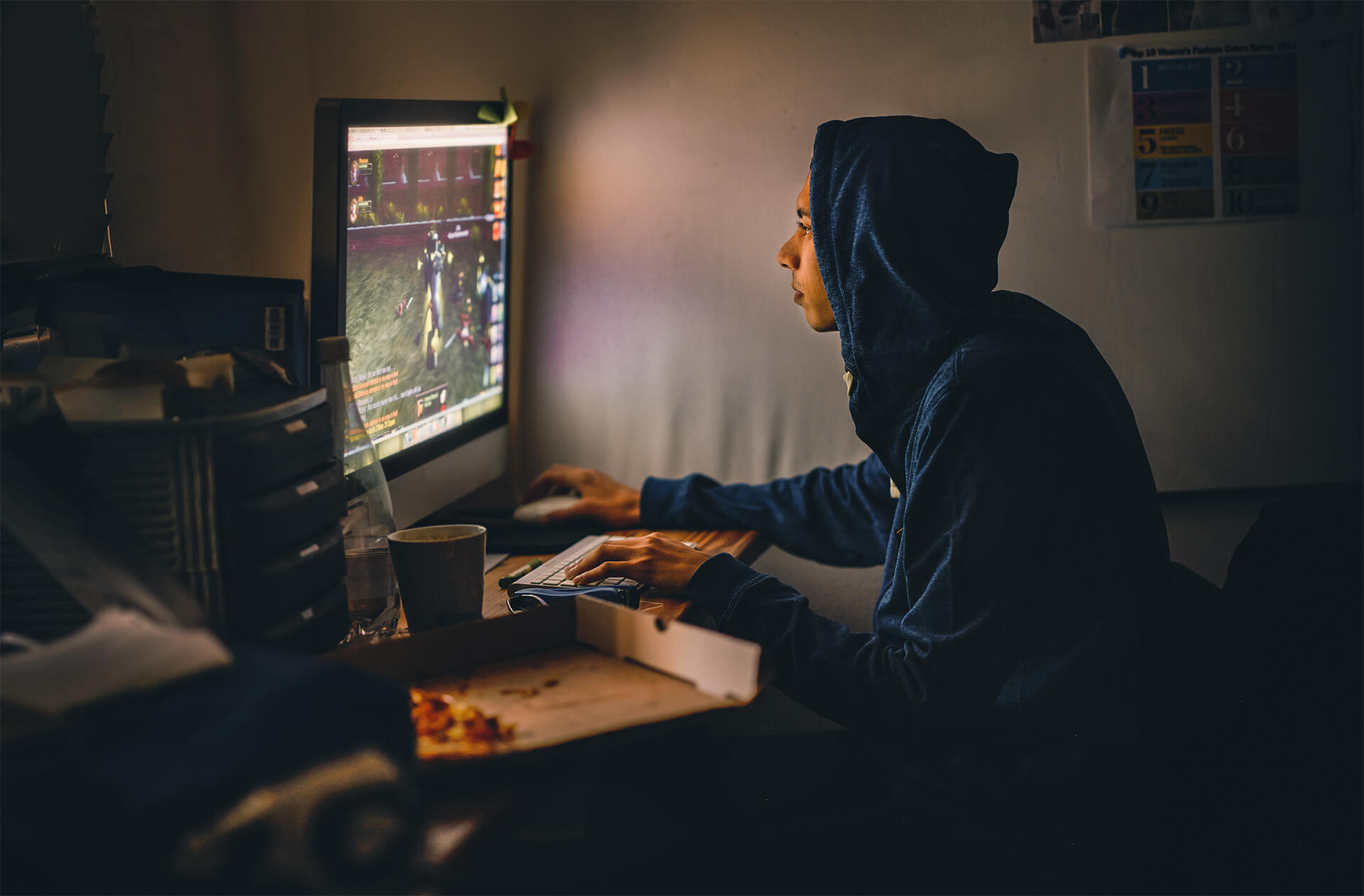 Jugendlicher sitzt in einem dunklen Zimmer und spielt ein Videospiel an seinem PC.