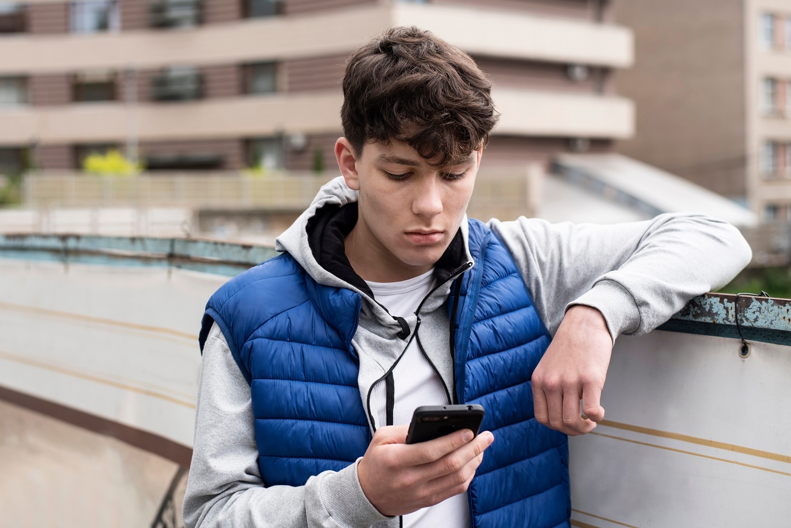 Jugendlicher lehnt an Mauer und guckt nachdenklich auf sein Smartphone